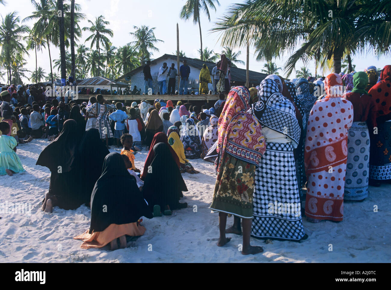 Les femmes et enfants portant des khangas regarder une scène en plein air dans l'événement festival du village de Paje à Zanzibar Banque D'Images