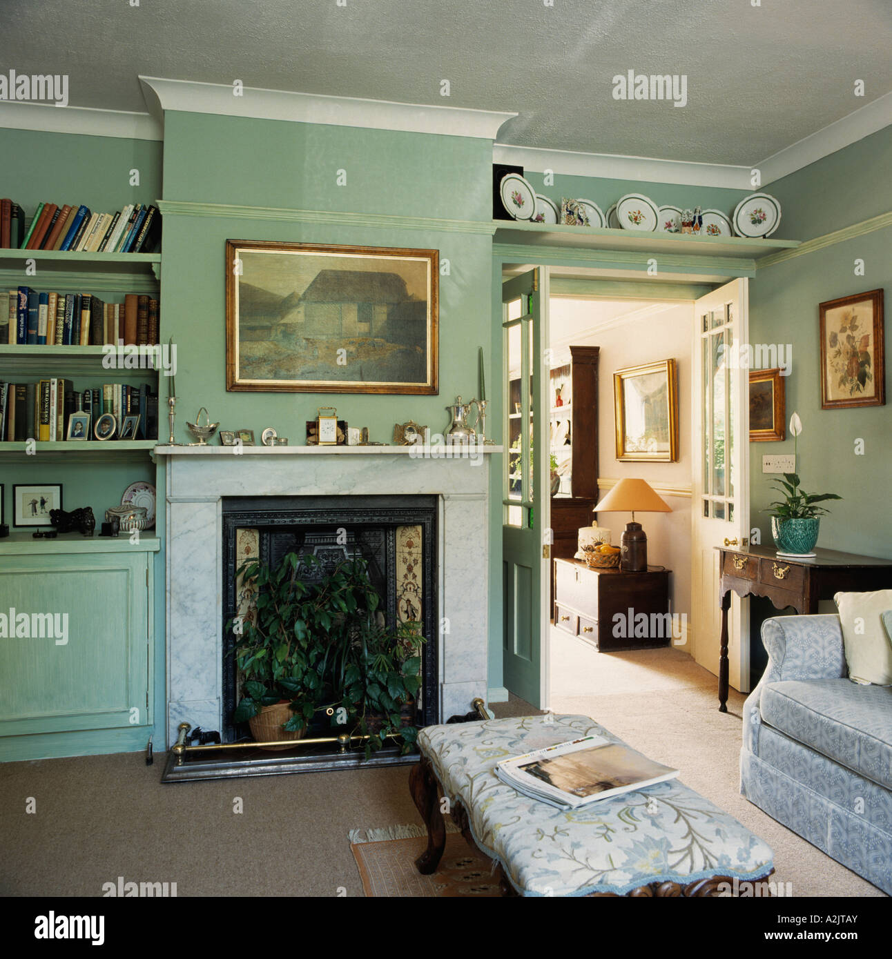 Photo au-dessus de cheminée en marbre avec foyer dans dans les plantes d'un vert pâle salon avec étagère au-dessus de portes à double vitrage Banque D'Images