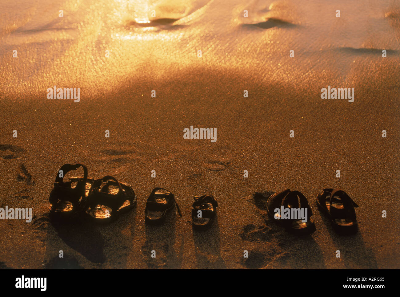 Famille de sandales sur sable au coucher du soleil Banque D'Images