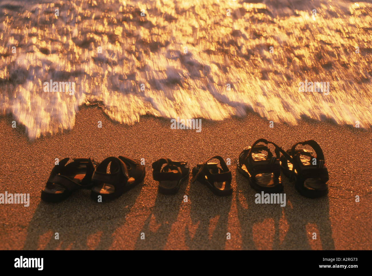 Famille de sandales sur sable au coucher du soleil Banque D'Images