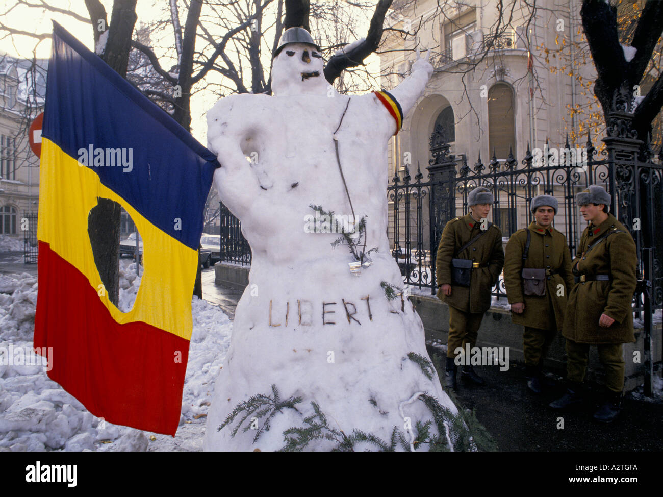 La Roumanie après la révolution trois soldats debout à côté de la liberté bonhomme thats tenant un drapeau roumain communiste avec le symbole des armoiries coupé Bucarest 1990 Banque D'Images