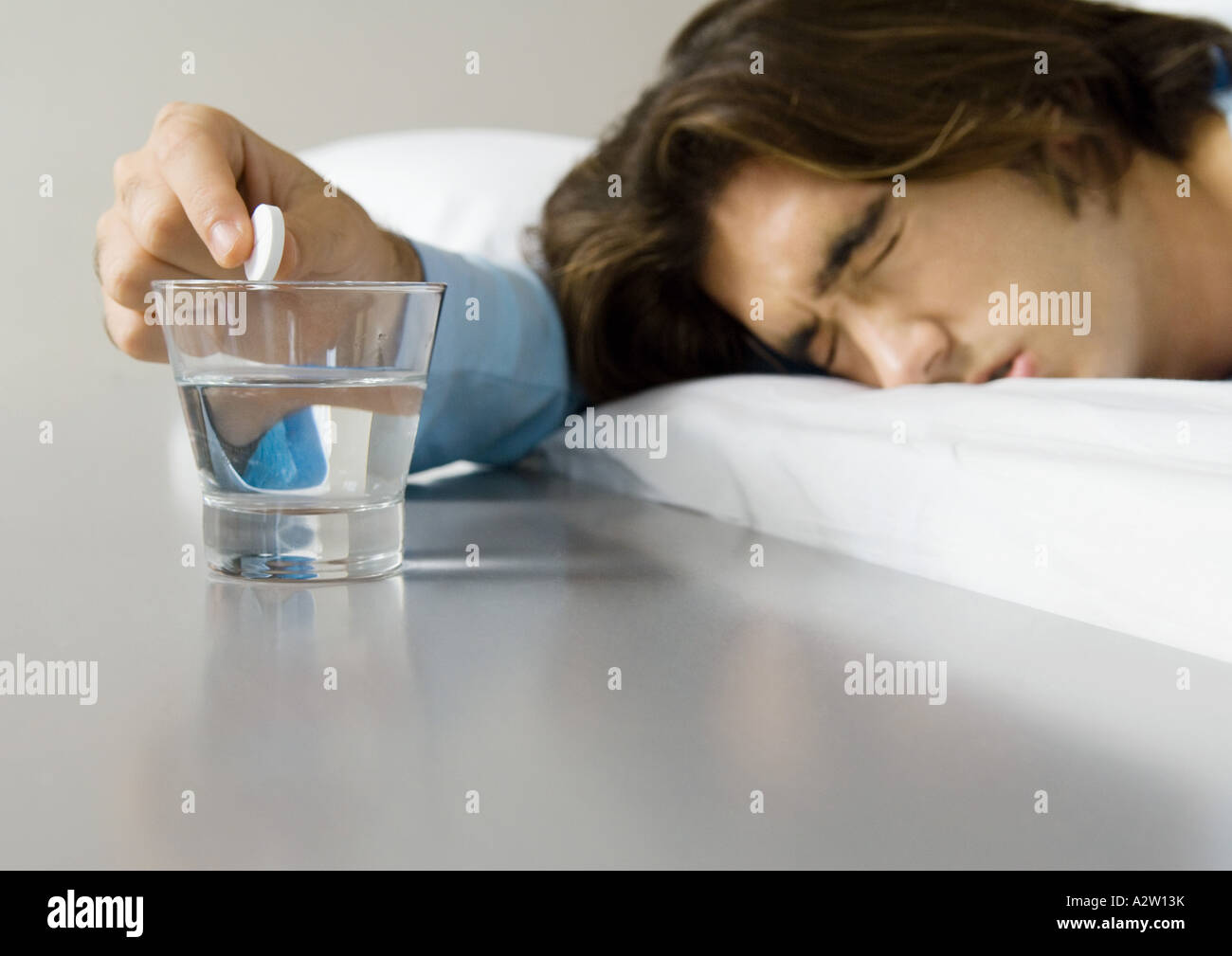 L'homme au lit, en plissant les yeux et en maintenant la médecine plus effervescent verre d'eau Banque D'Images