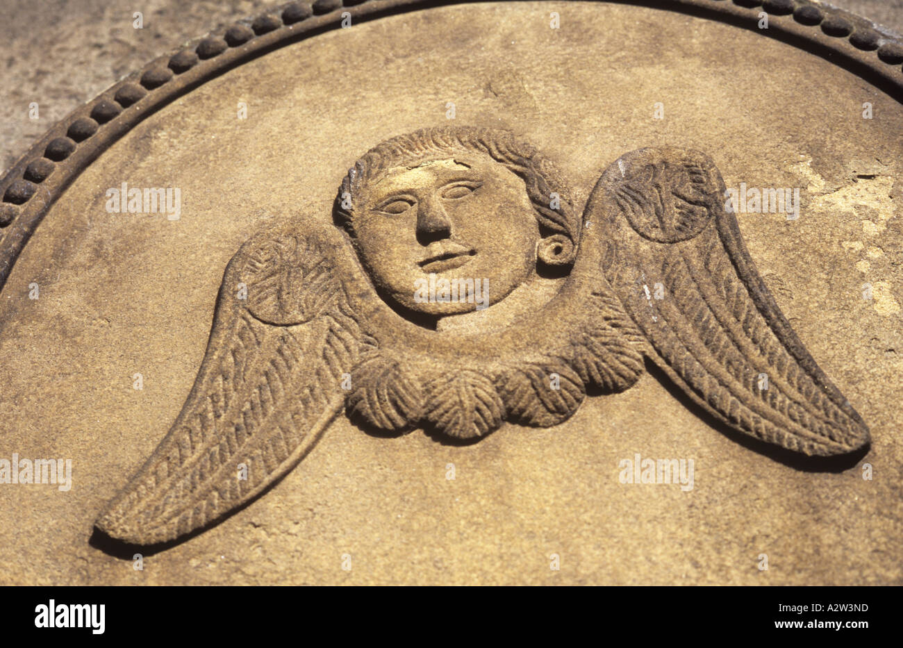 Détail de la pierre tombale en grès sculpté dans la lumière chaude de style naïf avec tête désincarnée et ailes d'un ange Banque D'Images