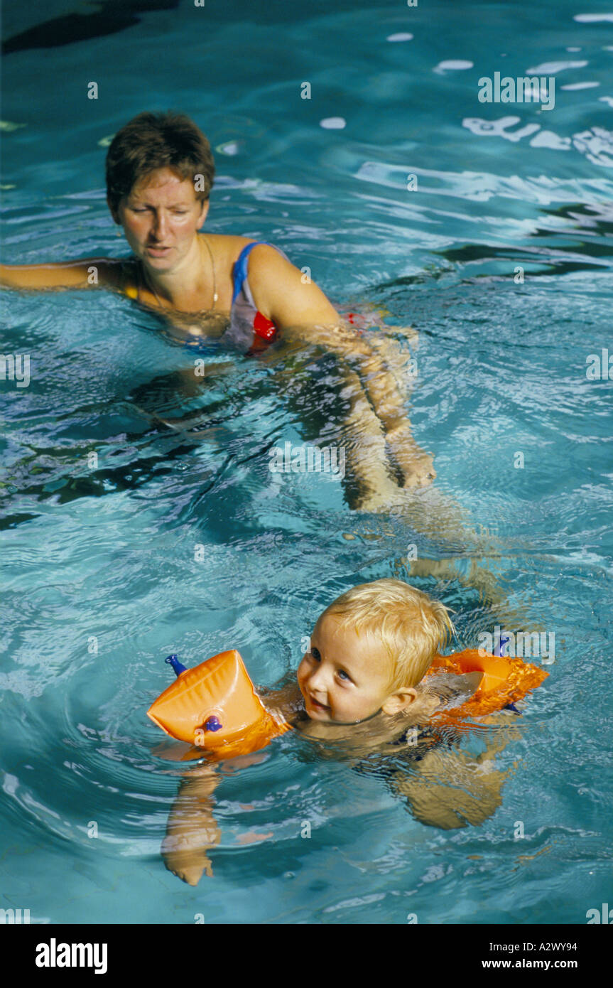 Une jeune mère aide son enfant à apprendre à nager dans une piscine portant des bandes de bras Banque D'Images