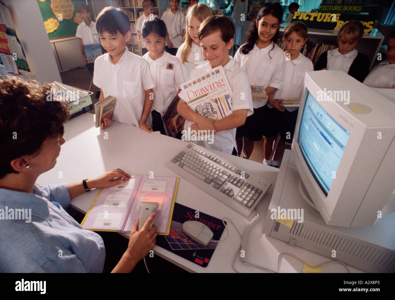 Enfants de l'école dans la bibliothèque.Bibliothécaire utilisant le lecteur de code-barres avec l'ancien ordinateur. Banque D'Images