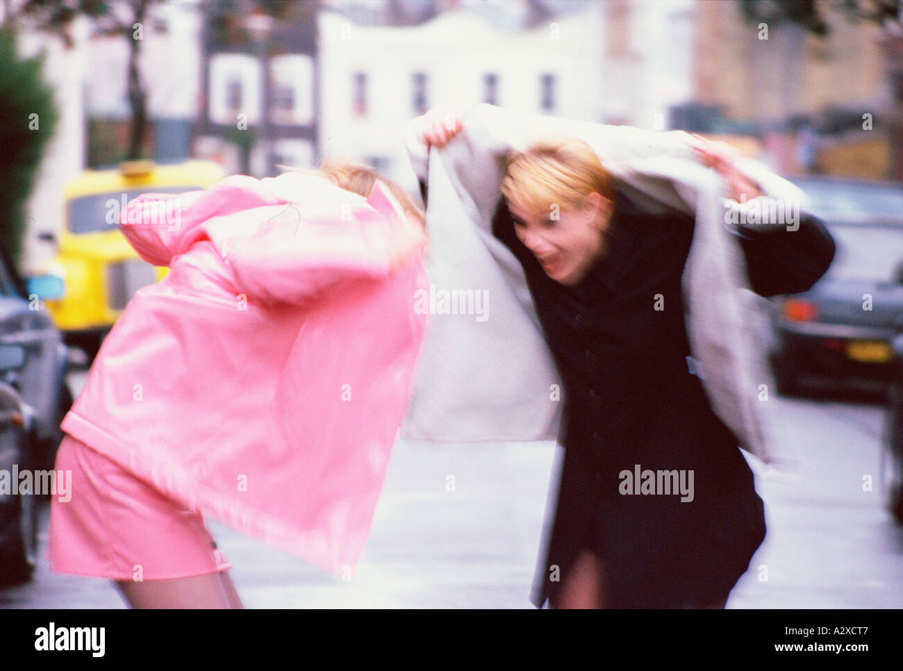 Impression de mouvement de deux jeunes femmes l'enfilage d'imperméables pris dans une averse soudaine. Londres. L'Angleterre Banque D'Images