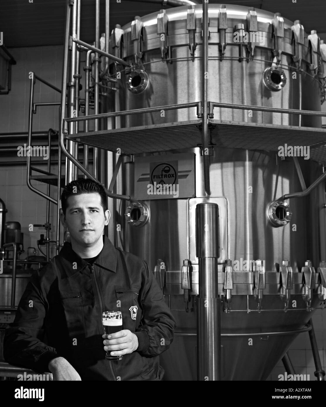 Brasserie travailleur ayant un verre de bière tout en devant une grande usine de filtration de la TVA d'une brasserie Banque D'Images