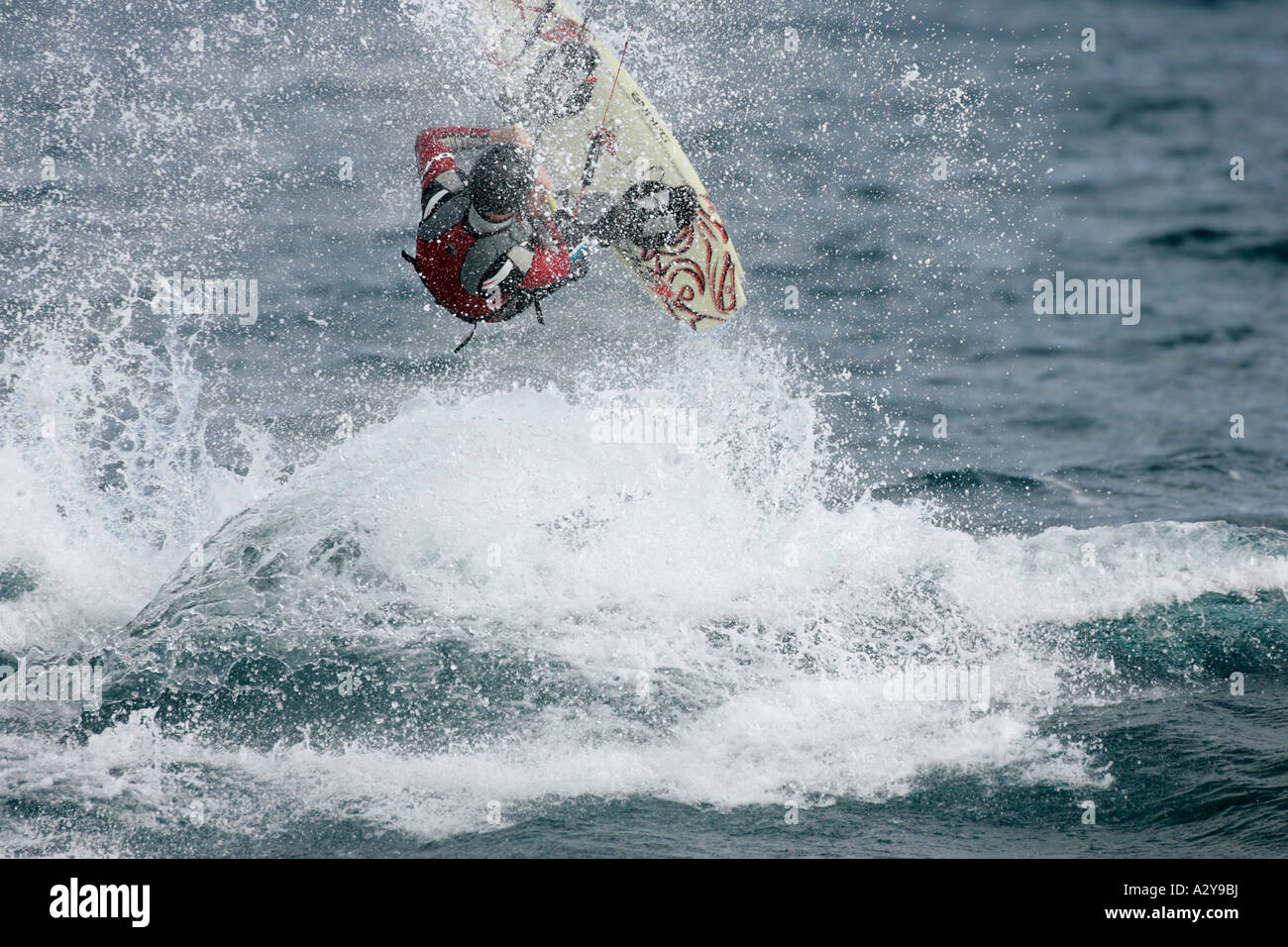 Homme kitesurfer en combinaison et casque lance son bord au large d'une vague à la vitesse dans la mer ce qui constitue une grosse splash Banque D'Images