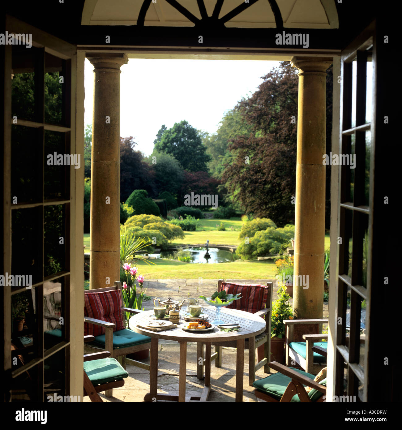 Voir à travers les portes doubles de piscine terrasse de jardin avec piliers, table et chaises Banque D'Images