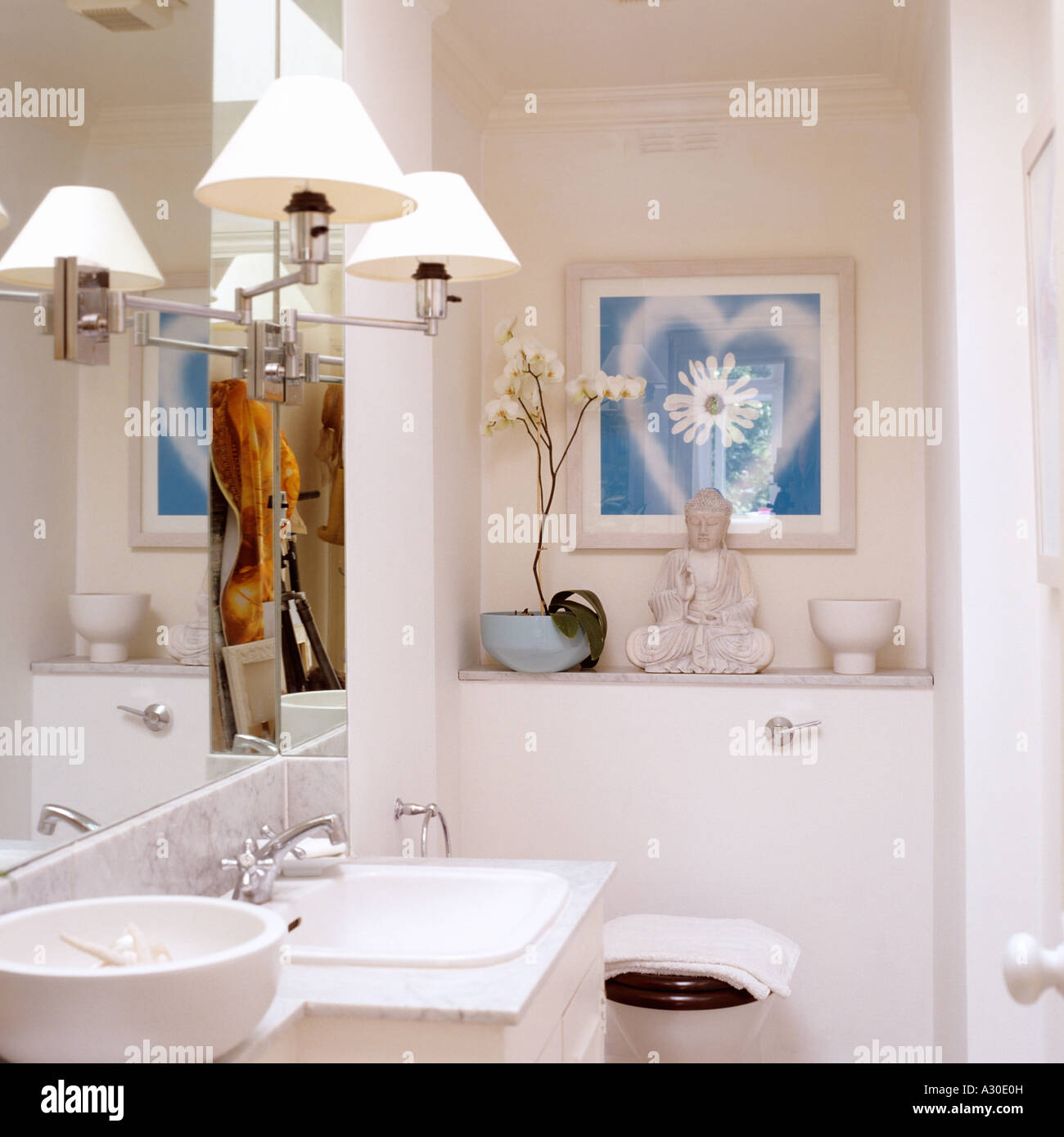 Lampes sur le miroir dans salle de bains laqué blanc avec statue de Bouddha et lavabo Banque D'Images