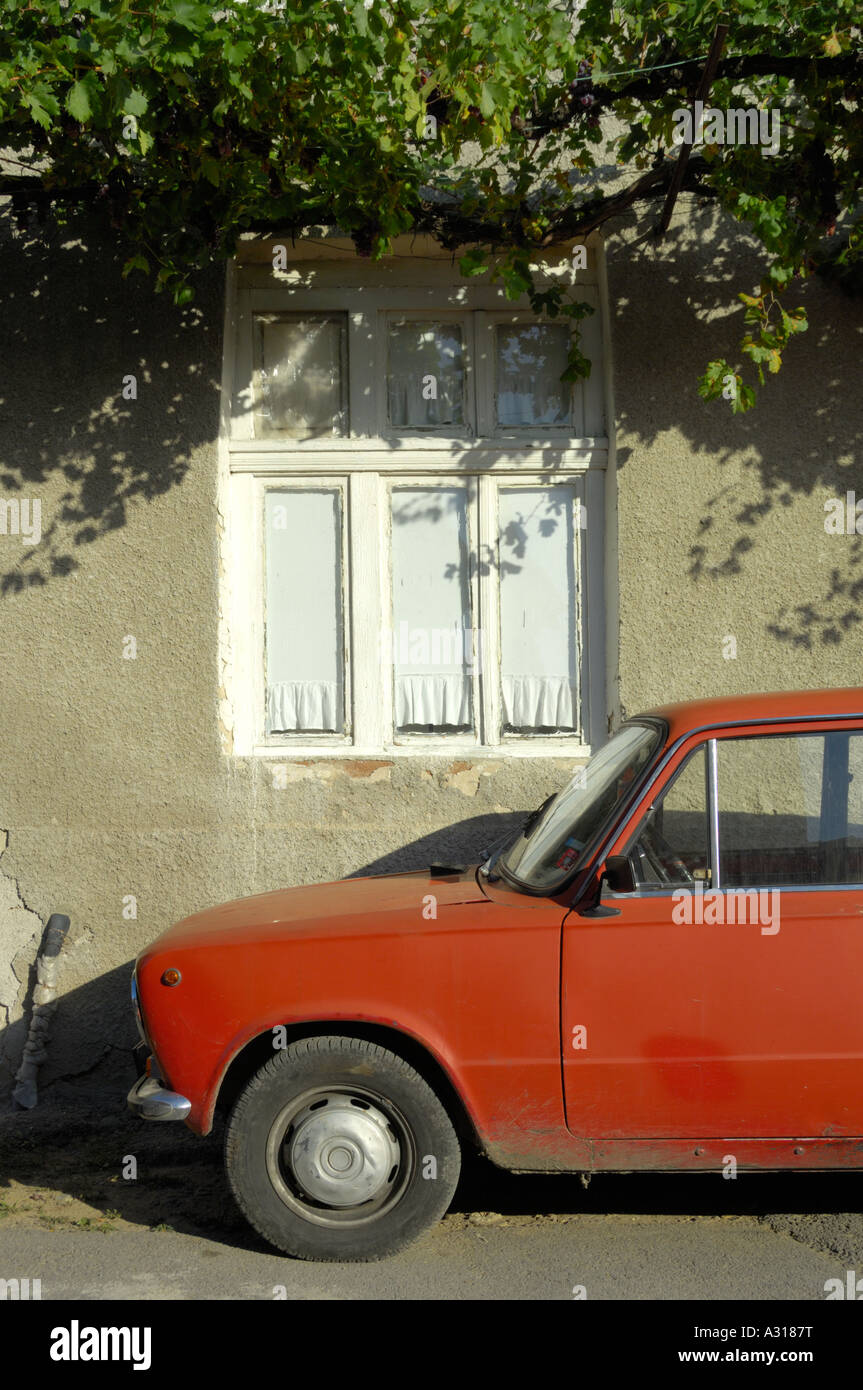 Scène de village bulgare ancienne Lada rouge voiture garée à l'extérieur couvert de vigne mur de plâtre de boue est de l'Europe Bulgarie Banque D'Images