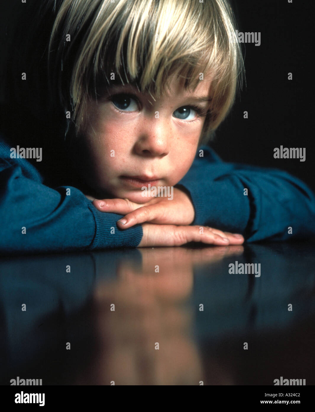 Portrait d'un petit garçon avec ses bras croisés et sa tête reposant sur le bureau Banque D'Images