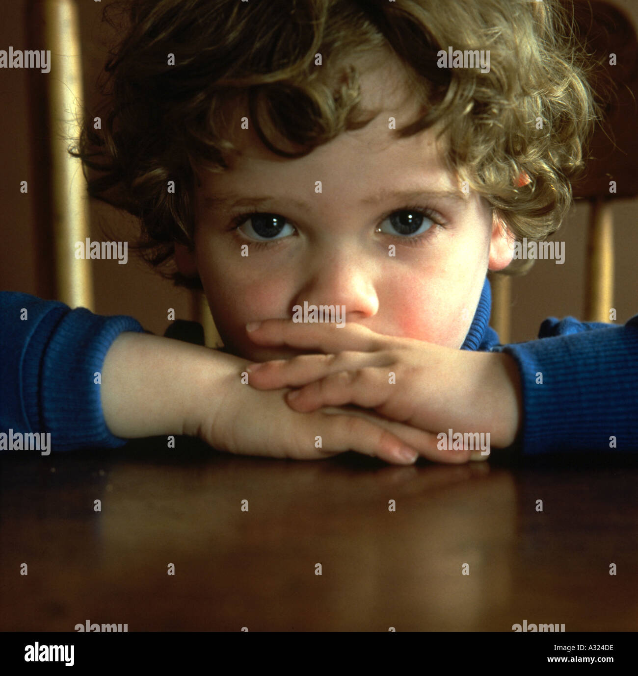 Jeune garçon avec les bras croisés sur la table et appuyant sa tête sur ses bras à directement à l'appareil photo Banque D'Images