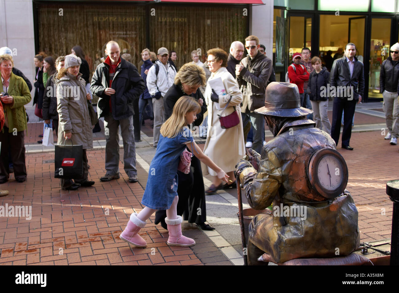 Les touristes se tenir autour de femme et de la jeune fille donnent de l'argent à street performer vêtue comme une statue de métal Banque D'Images