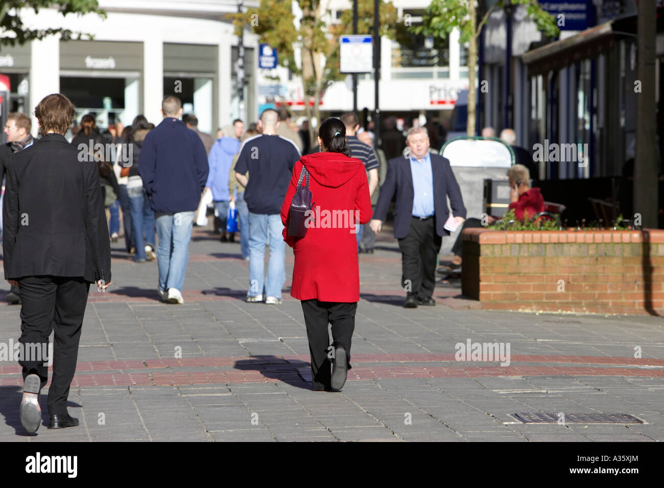 Femme en rouge long manteau promenades le long des rues piétonnes pavées de briques occupé dans Belfast City Centre Banque D'Images
