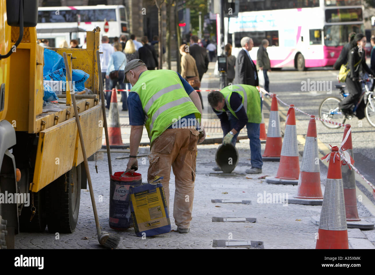 Ouvriers constructeurs dans la réparation des gilets haute visibilité zone pavée en dehors de Belfast City Hall avec yellow lorry et cônes Banque D'Images
