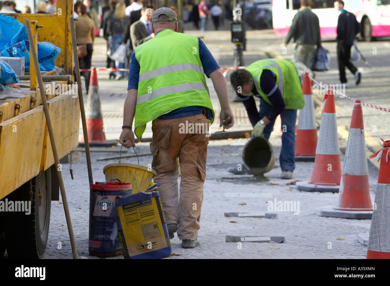 Ouvriers constructeurs dans la réparation des gilets haute visibilité zone pavée en dehors de Belfast City Hall avec yellow lorry et cônes Banque D'Images