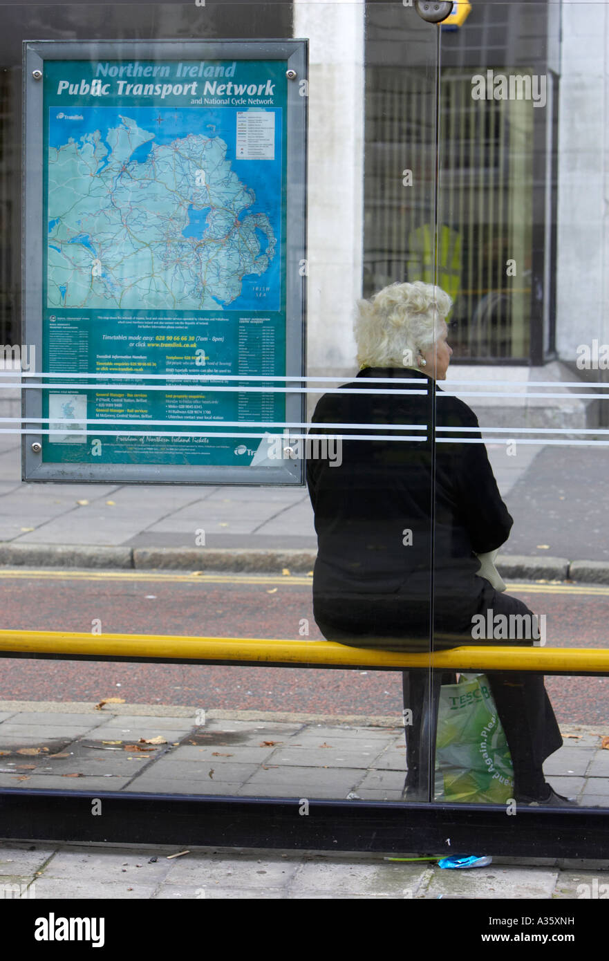 Vieille Femme aux cheveux gris se trouve à l'arrêt de bus avec tescos sac shopping recyclable en attente d'un bus dans le centre-ville de Belfast Banque D'Images