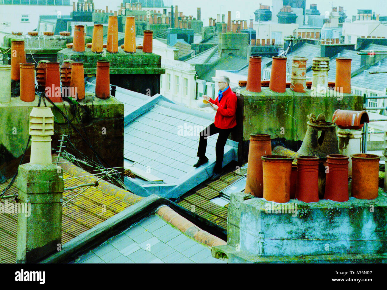 Sur le toit un artiste dessine un paysage urbain entre les ardoises et tuiles. Banque D'Images