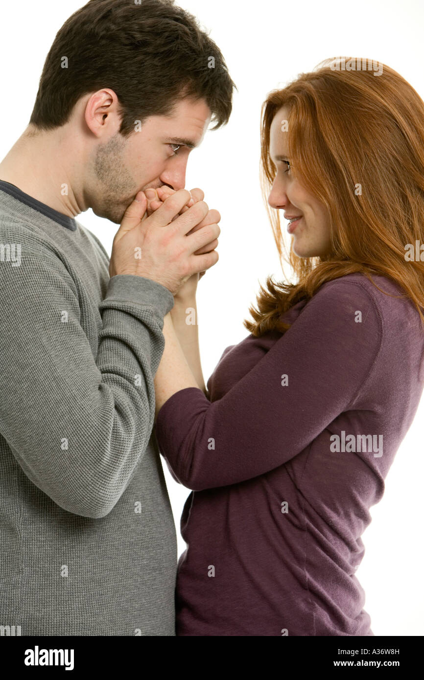 Jeune homme embrasse les doigts de sa belle petite amie rousse dans un bref moment intime comme ils regardent fixement dans les yeux Banque D'Images