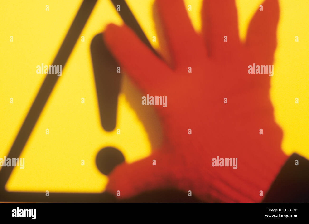 Une main gantée rouge flou apparaissant de tenir une exclamation roadsign sur son fond jaune Banque D'Images