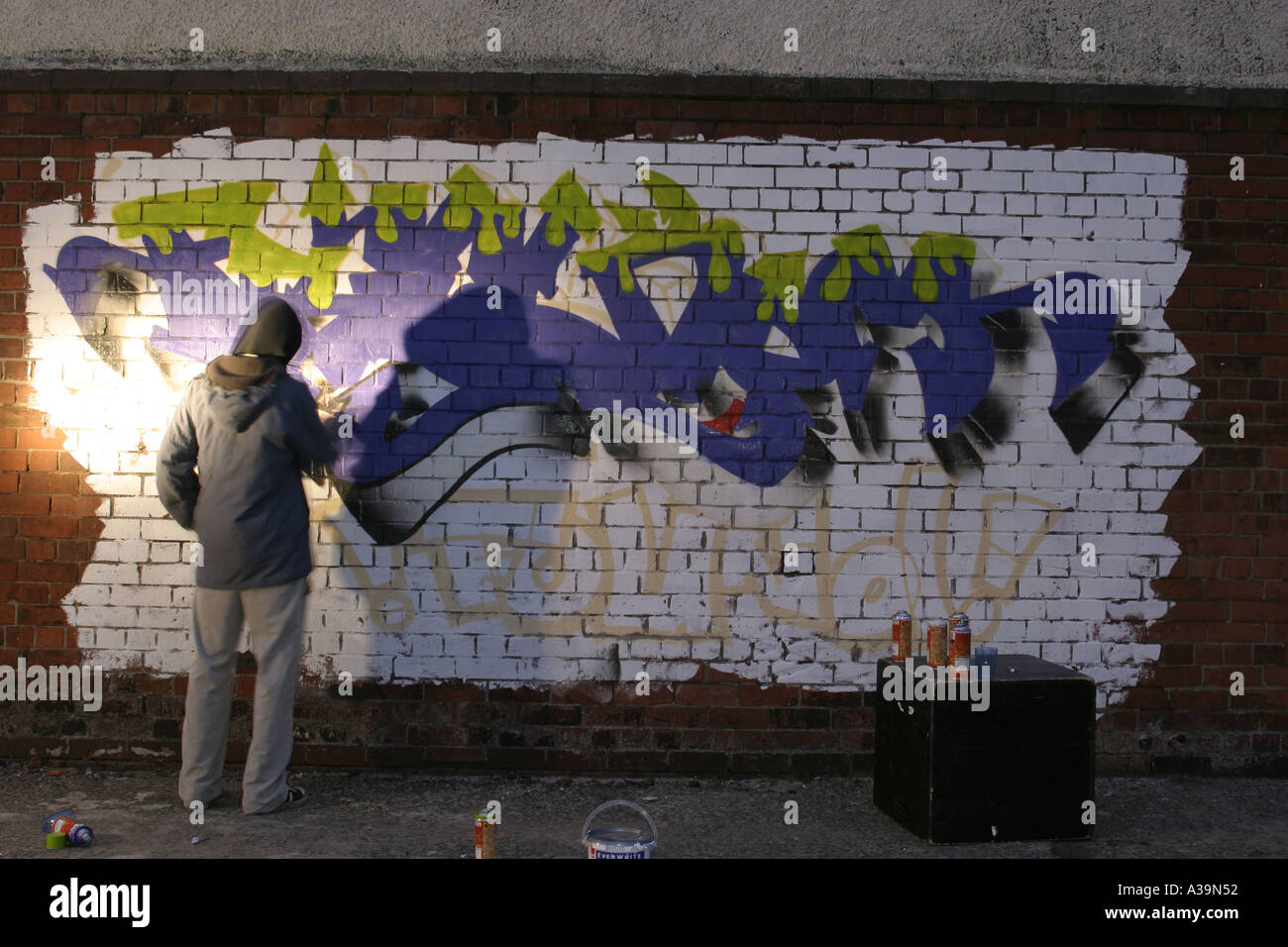 Graffiti Tag artiste au travail avec la peinture en aérosol peut porter haut à capuchon de protection et masque de visage de l'Irlande du Nord Belfast Banque D'Images