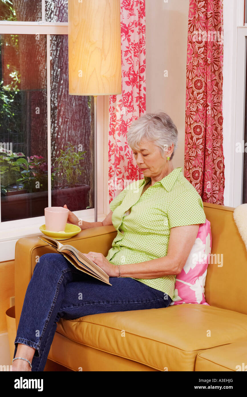 Senior woman sitting on a couch et la lecture d'un livre Banque D'Images