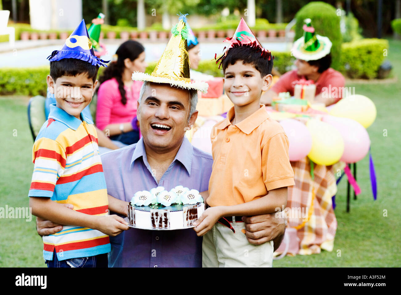 Deux garçons debout avec leur père et la tenue d'un gâteau d'anniversaire Banque D'Images