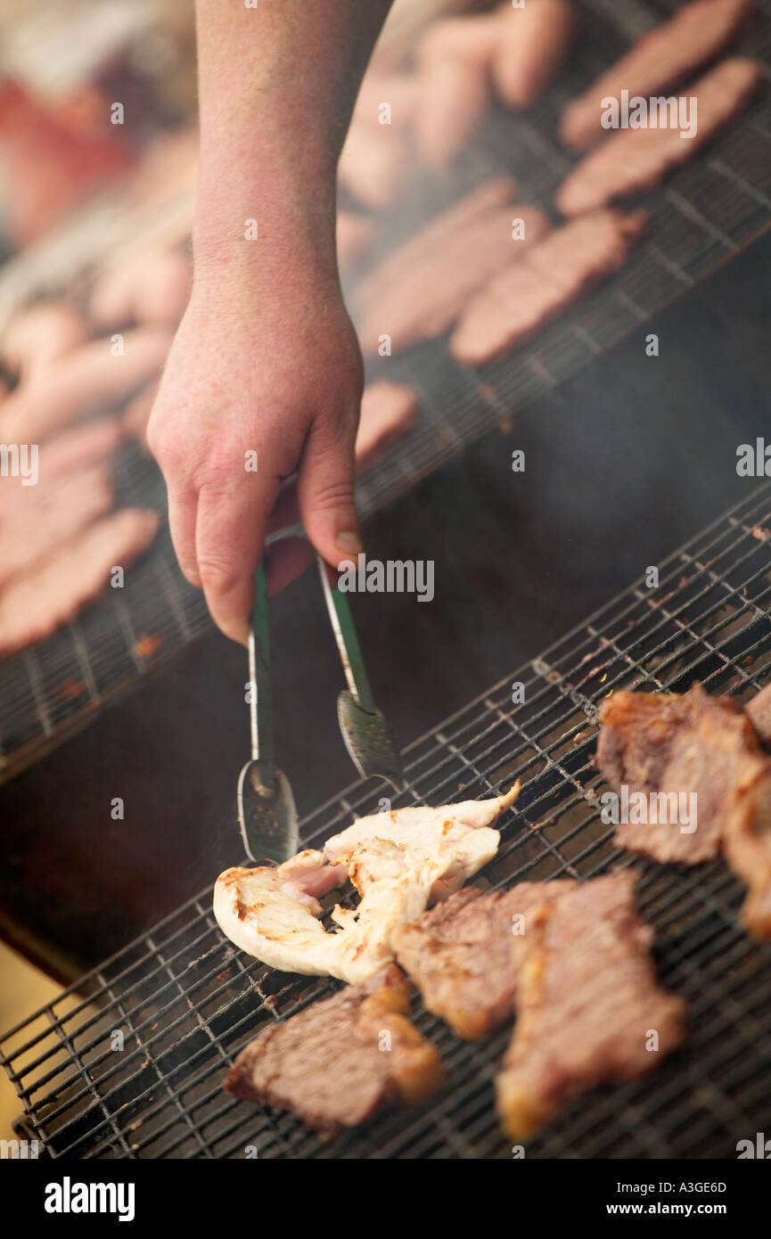 STEAKS DE BOEUF ET POULET CUISSON SUR UN BARBECUE AVEC DES HAMBURGERS EN ARRIÈRE-PLAN Banque D'Images