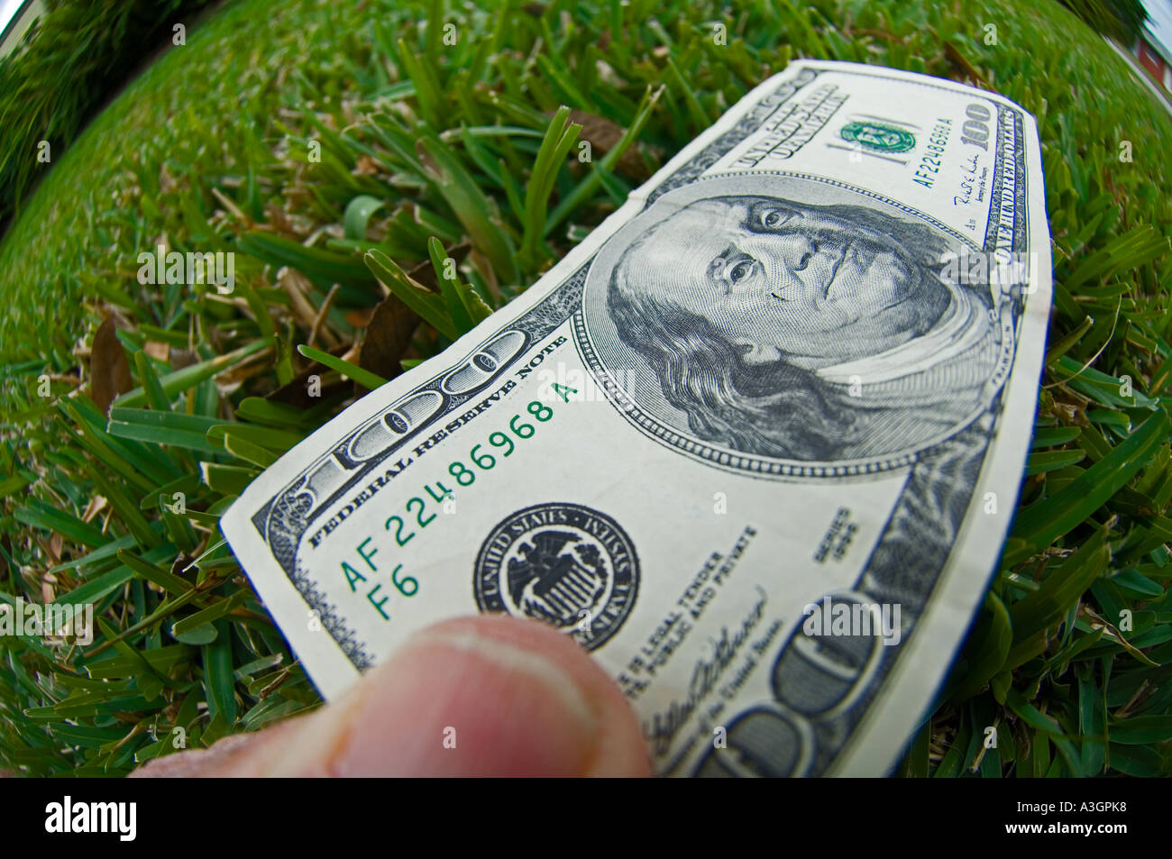 Fish eye view of hand prise d'une centaine de dollars US sur la pelouse Banque D'Images