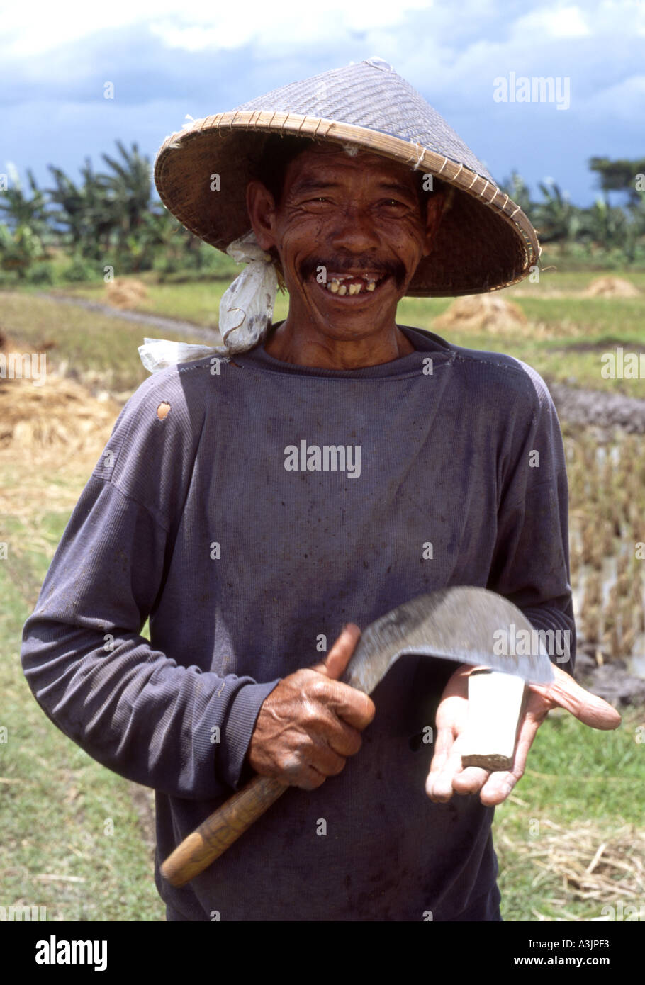 Smiling elderly travailleur d'un grand nombre de ses dents son repas d'un serpent dans un sac suspendu à son chapeau conique Madiun East Java Banque D'Images