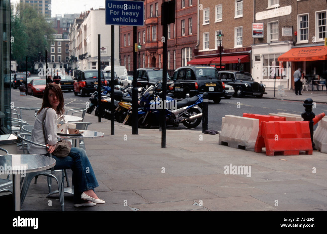 Scène de rue ordinaire à Londres en Angleterre avec les taxis motos en stationnement travaux routiers et d'une femme assise à une table de café à l'extérieur Banque D'Images