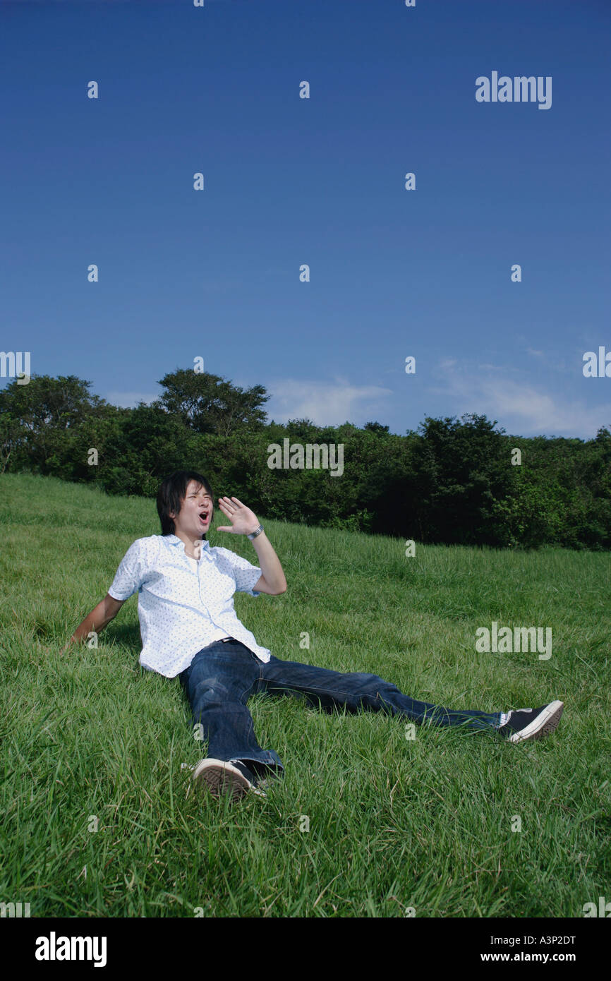 Un jeune homme assis sur l'herbe et les cris Banque D'Images