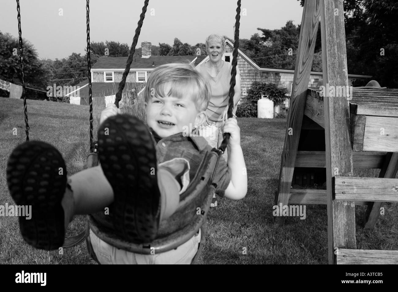 Enfant le swing avec les pieds dans l'appareil photo grand-mère femme derrière lui en poussant Banque D'Images