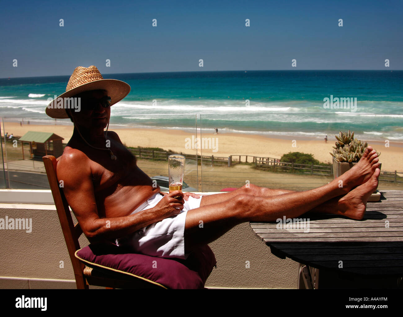 A mettre en place et bien tannés mais middle aged homme boit une bière au soleil avec une vue sur la plage de Curl Curl et surf Sydney Australie Banque D'Images