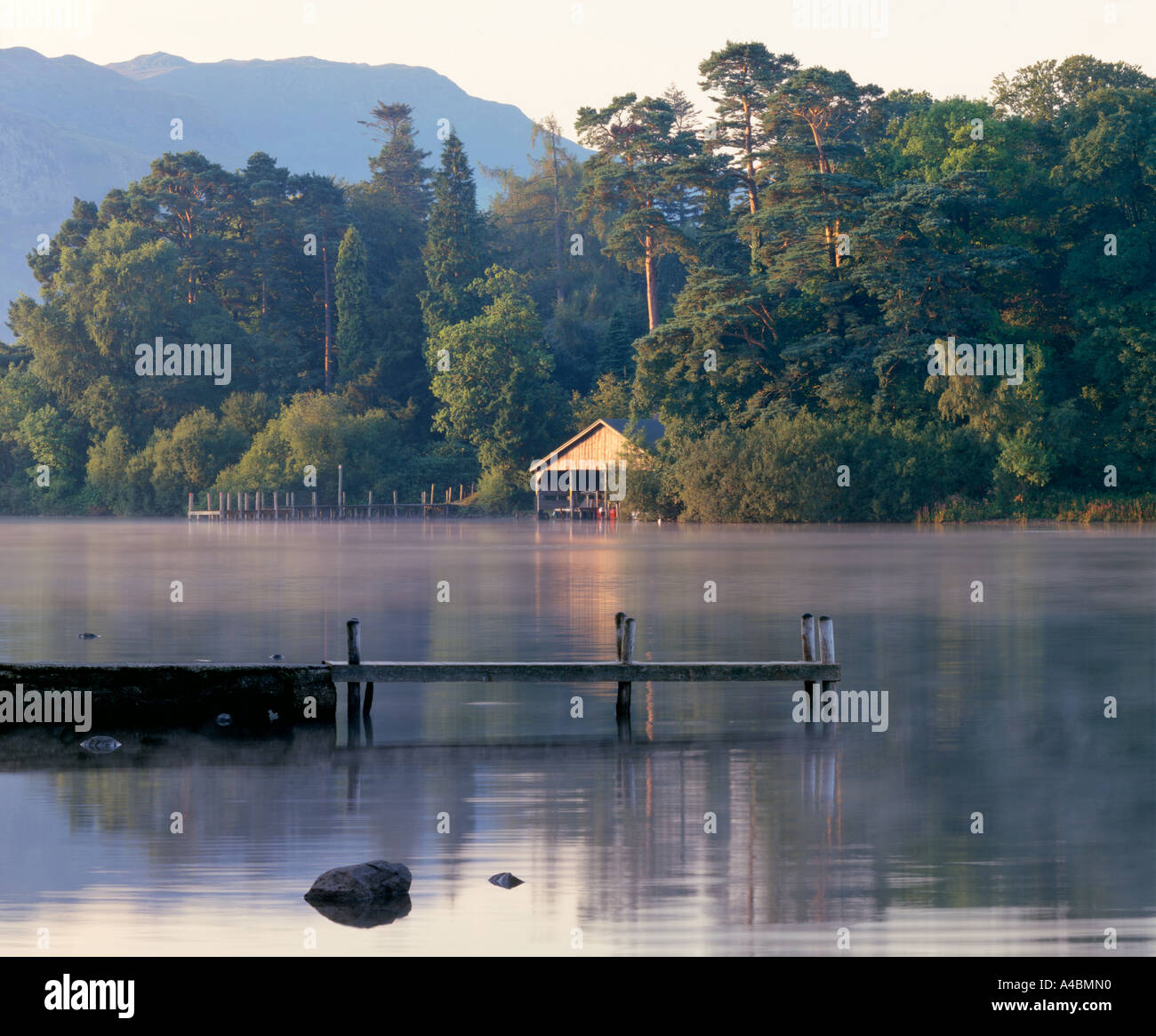 A sunlit boathouse encadrée par des arbres matures sur le lac Derwent dans le Lake District avec brouillard étendu sur le lac et d'une jetée Banque D'Images