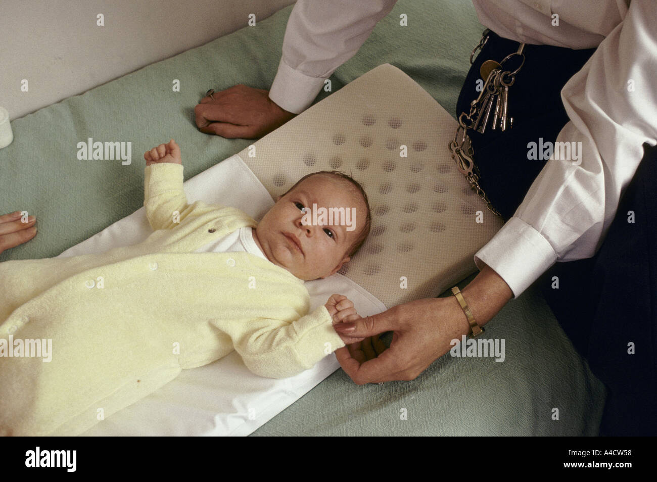 Un bébé se trouve sur un lit, des montres par un officier de la prison. Banque D'Images