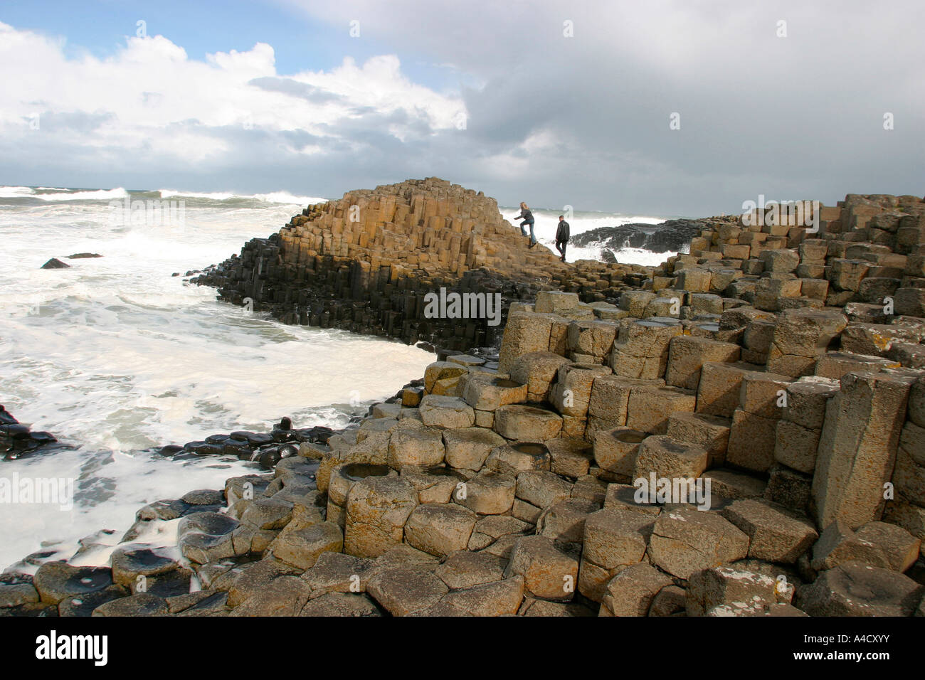 Le comté d'Antrim Giants Causeway couple climbing sur rochers entourés par de gros surf Banque D'Images