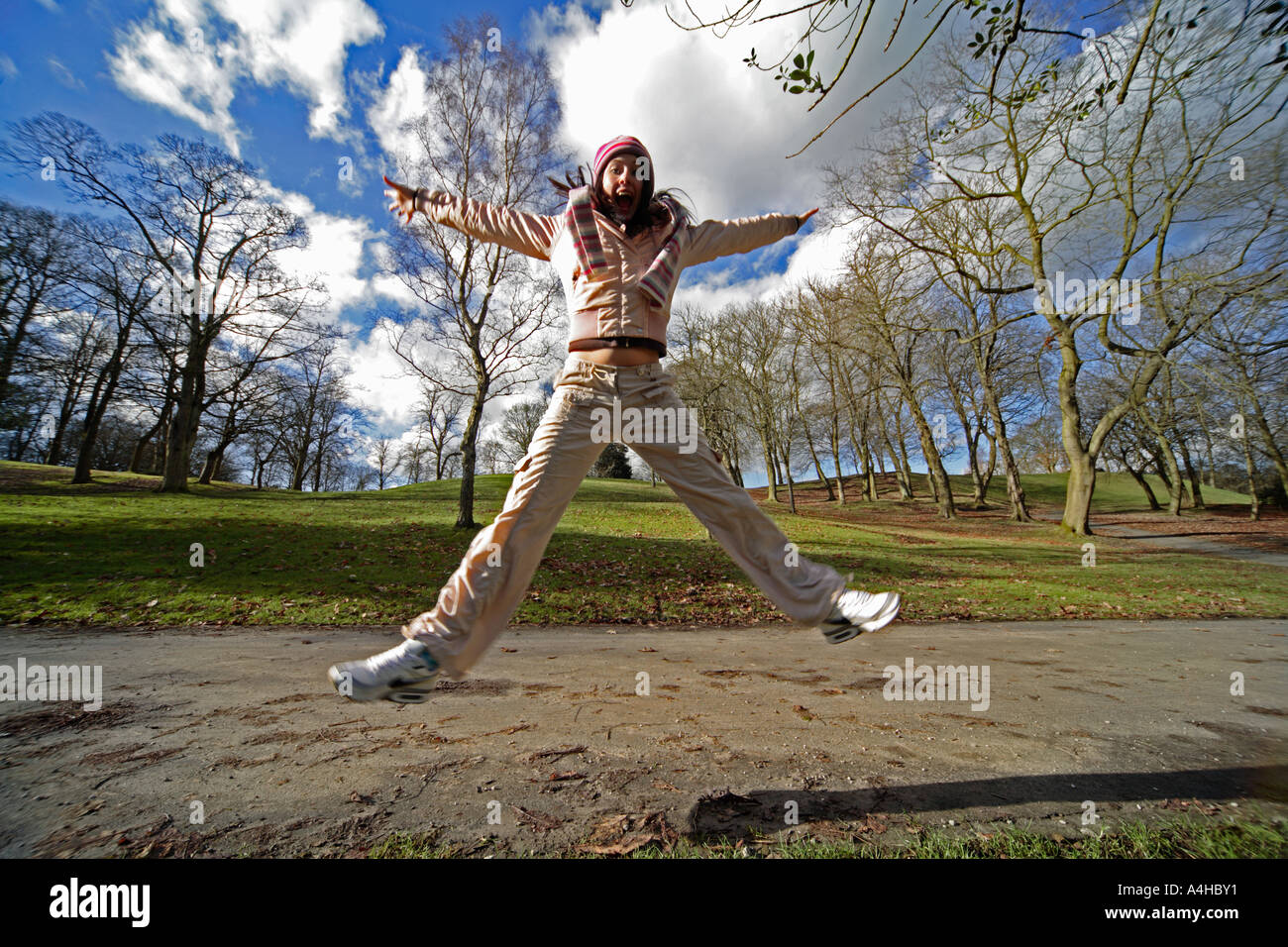 Grand angle dynamique et coloré de l'action de jeune fille de 16 ans faisant un coup de ciseaux, plein d'énergie dans un parc avec des arbres Banque D'Images