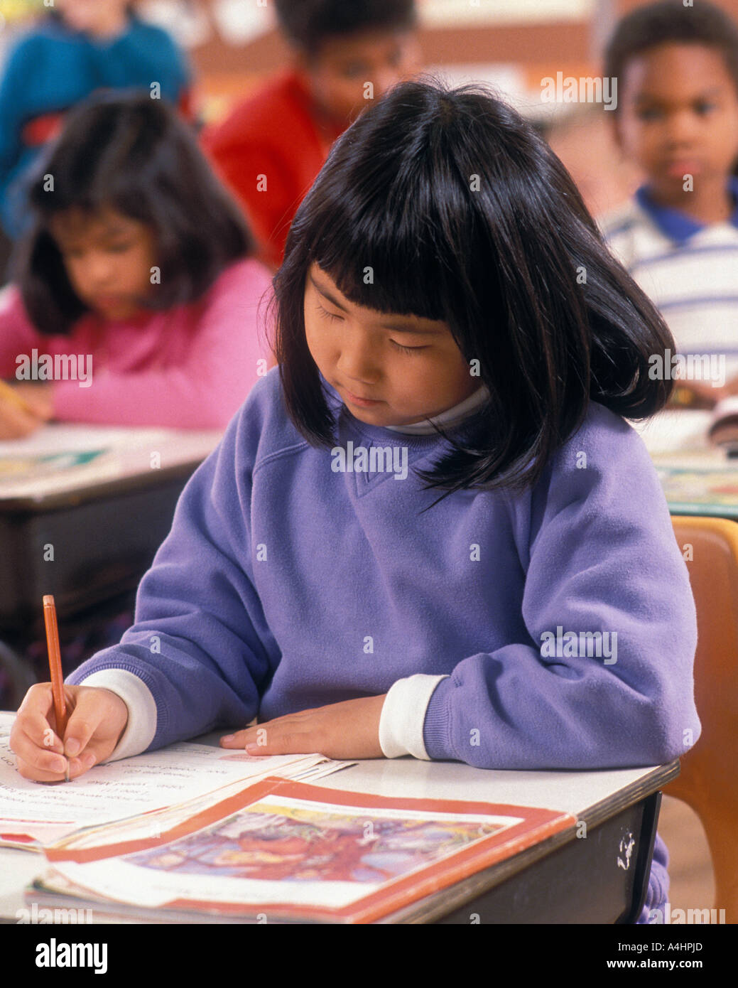 Asian girl sitting at desk praticing écrit à l'école primaire non trouvé verticale Banque D'Images
