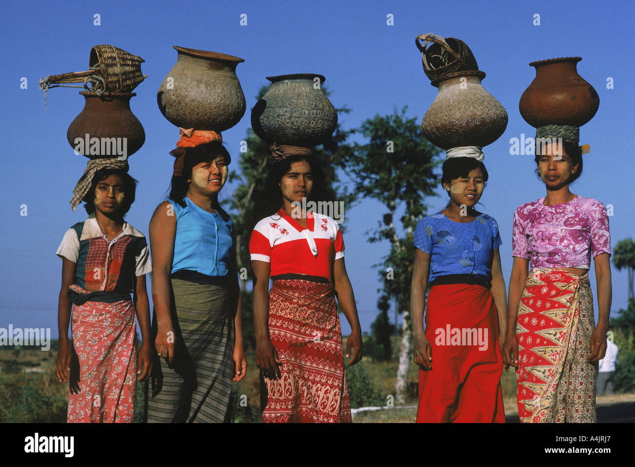 Les femmes avec un bloc solaire creme sur leurs visages transportant des pots d'argile remplis d'eau au Myanmar Banque D'Images