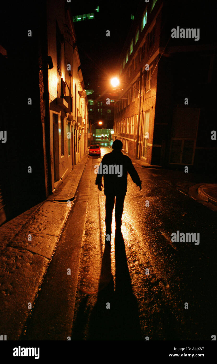 La forme sombre d'un homme solitaire dans une rue de ville de nuit. Banque D'Images