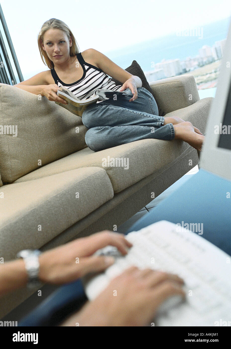 Woman relaxing on sofa, les mains sur le clavier en premier plan Banque D'Images
