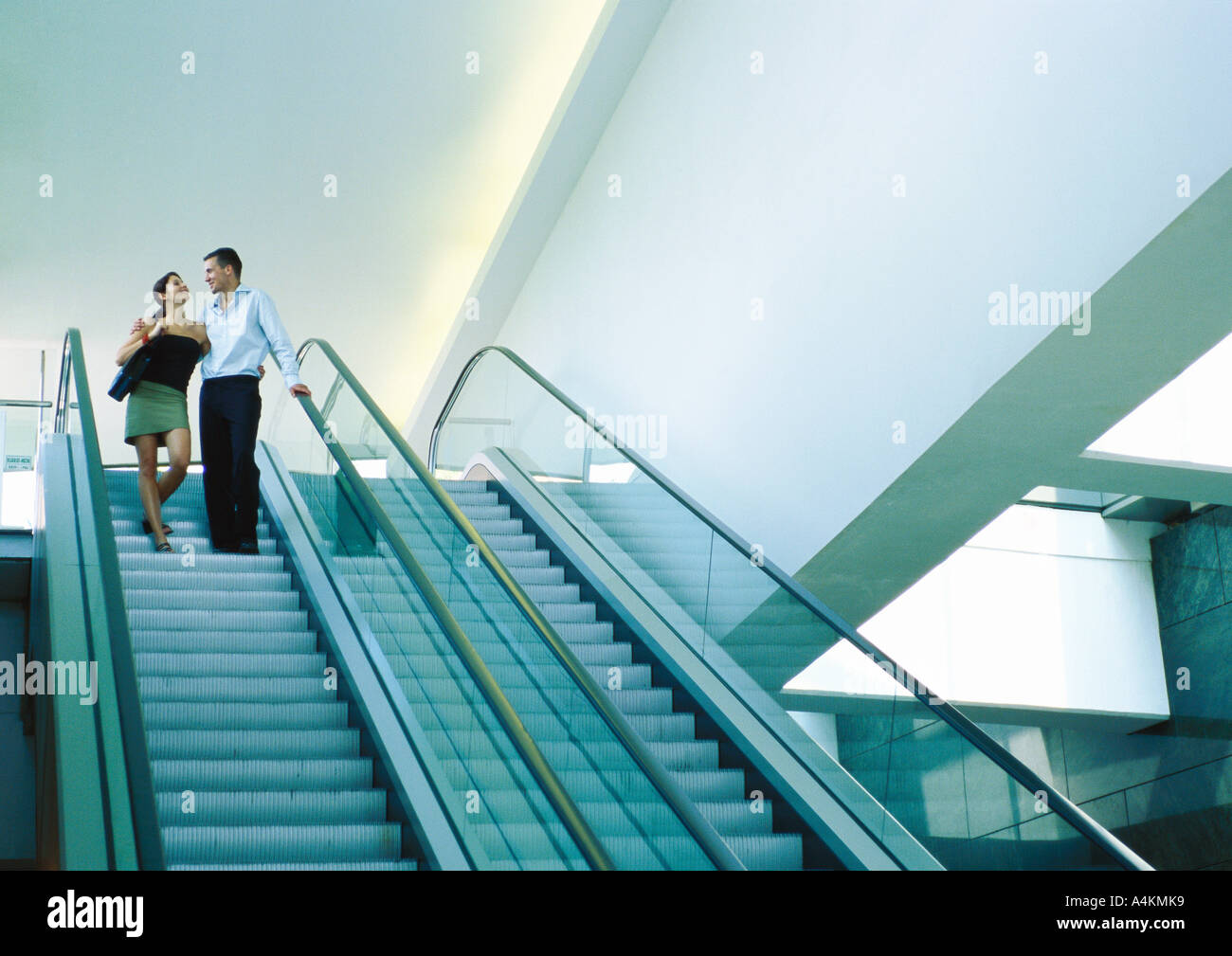 Couple riding down escalator, smiling Banque D'Images