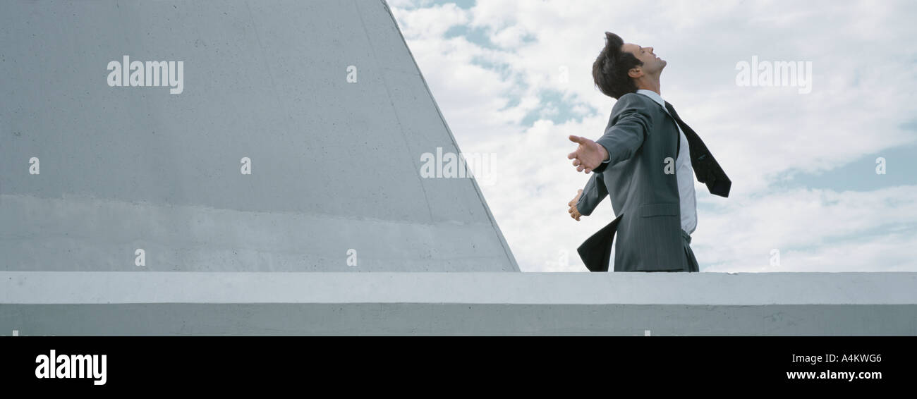 Homme debout derrière mur de béton avec les bras tendus, side view Banque D'Images
