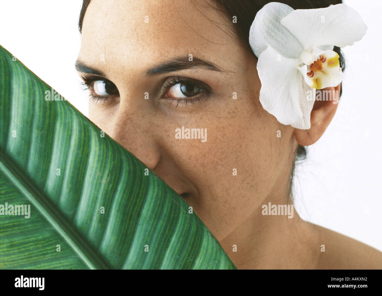 Femme avec orchidée derrière l'oreille, la feuille de palmier couvrant partiellement le visage, close-up Banque D'Images