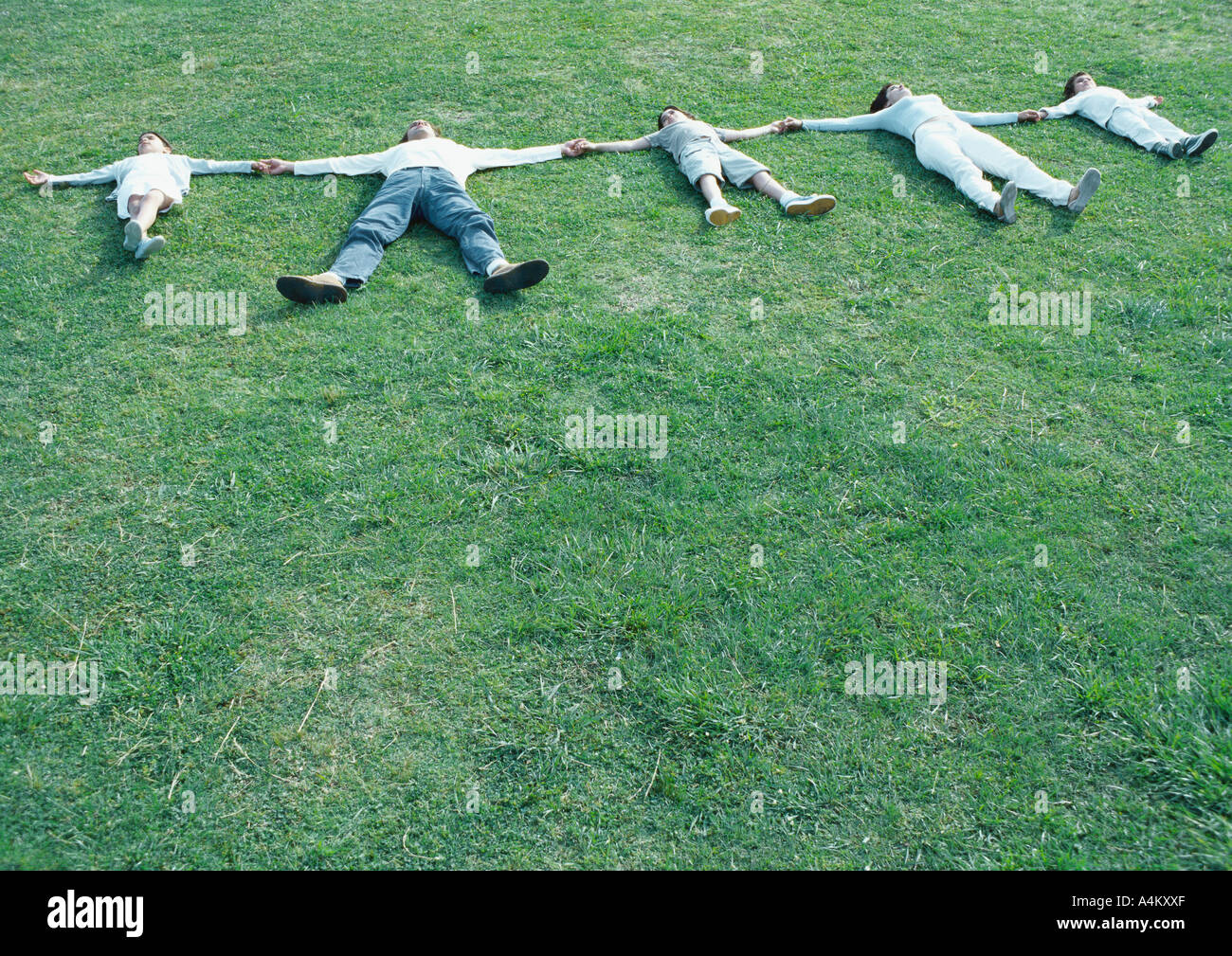 Les parents avec les garçons et filles allongé sur dos à l'herbe avec les bras, se tenant la main Banque D'Images
