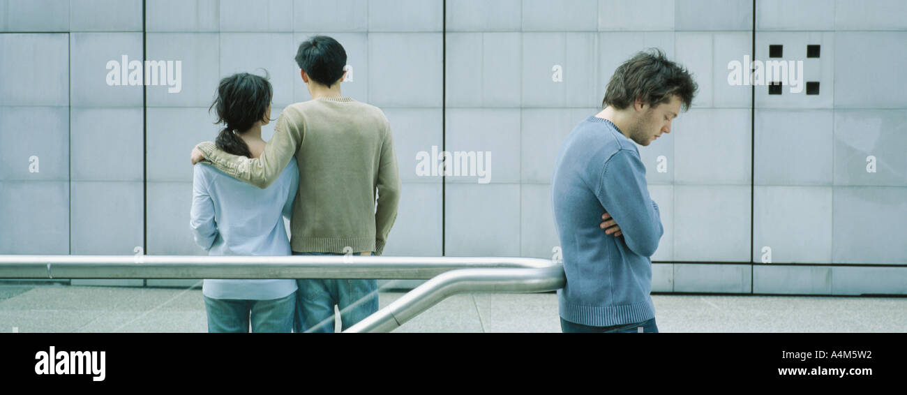 Jeune couple en train de marcher ensemble, jeune homme debout avec les bras croisés en premier plan Banque D'Images