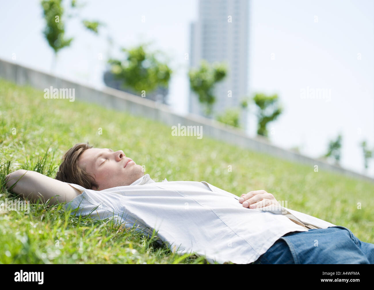 Young man lying on grass in urban park Banque D'Images