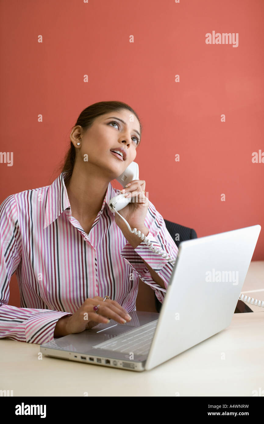 Businesswoman talking on phone while using laptop Banque D'Images